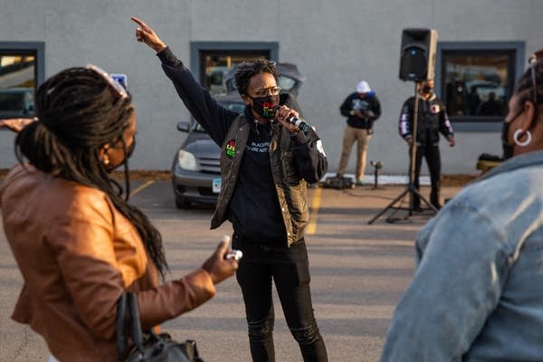 A woman points in the air and speaks into a microphone.